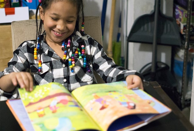 Girl smiling reading reading a black history book for children