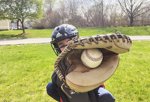 Kid in a baseball helmet catches a ball with a baseball glove