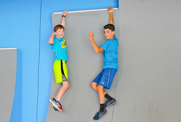 Photo of two children hanging from an obstacle course wall.