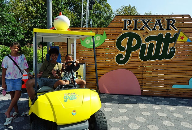 Three kids post with Pixar Putt golf cart and logo
